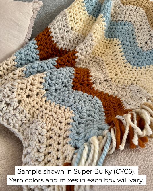 Crocheted blanket with a zigzag pattern in neutral colors on a couch.