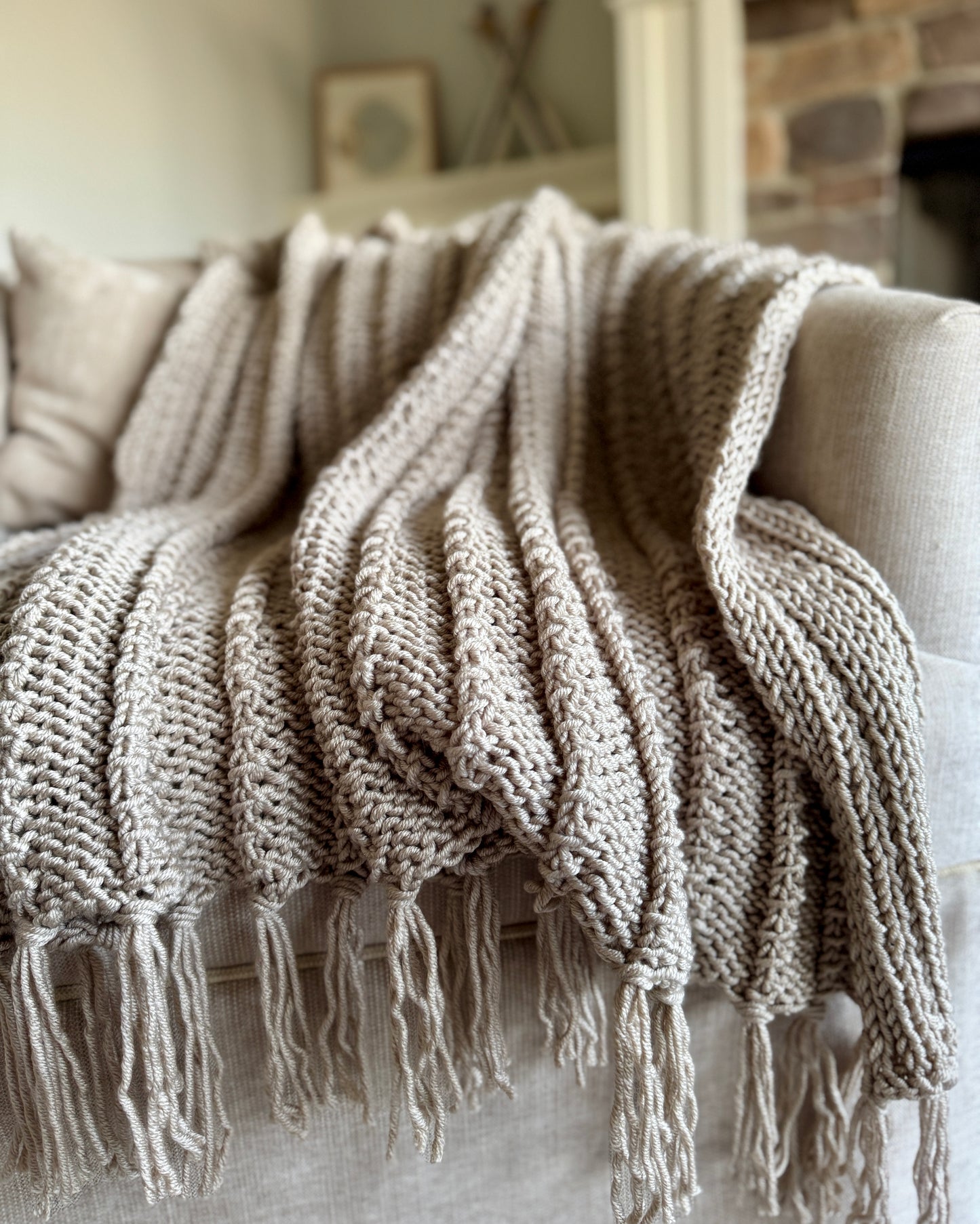 Knitted blanket with tassels draped over a sofa in a cozy living room.
