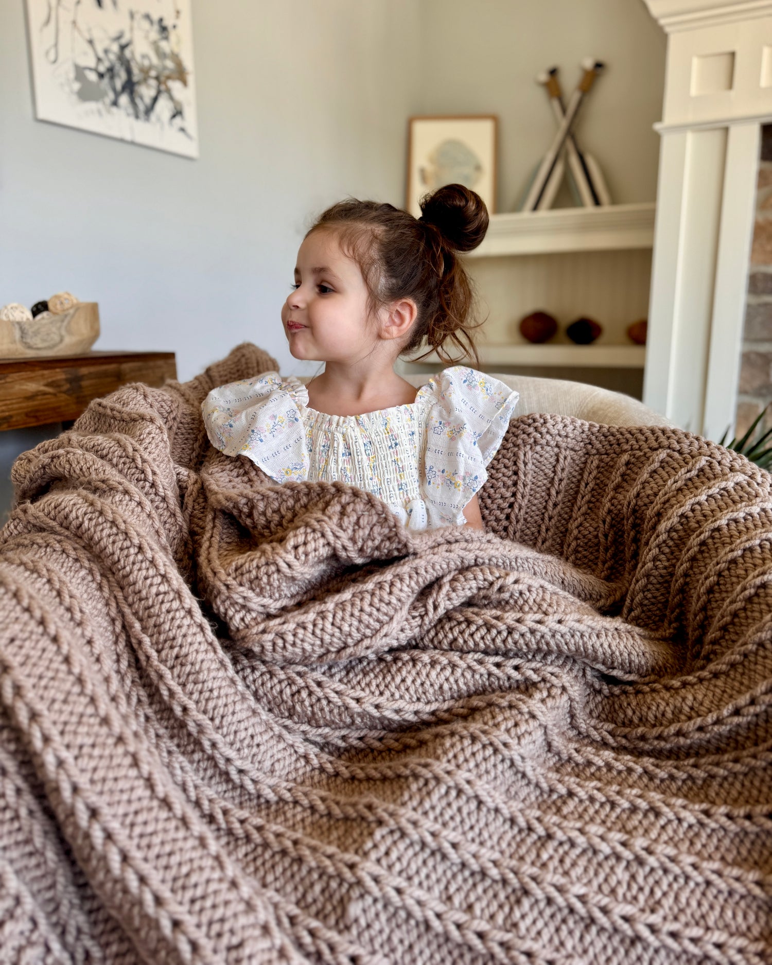 Child sitting in a cozy basket with a textured blanket, in a home setting.