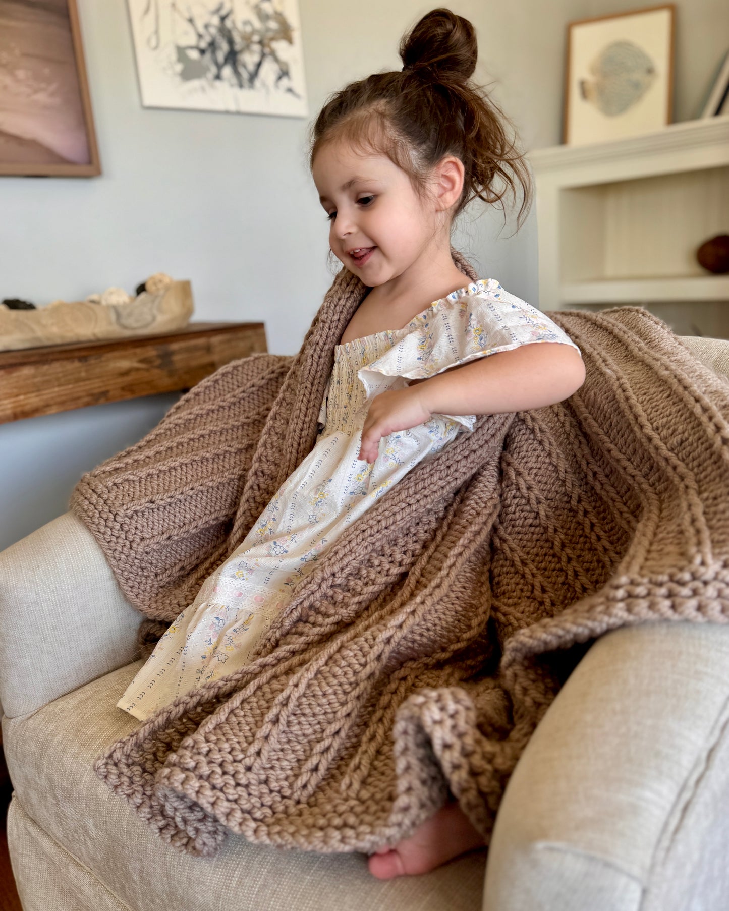 Young girl sitting on a couch with a brown knitted blanket draped over her