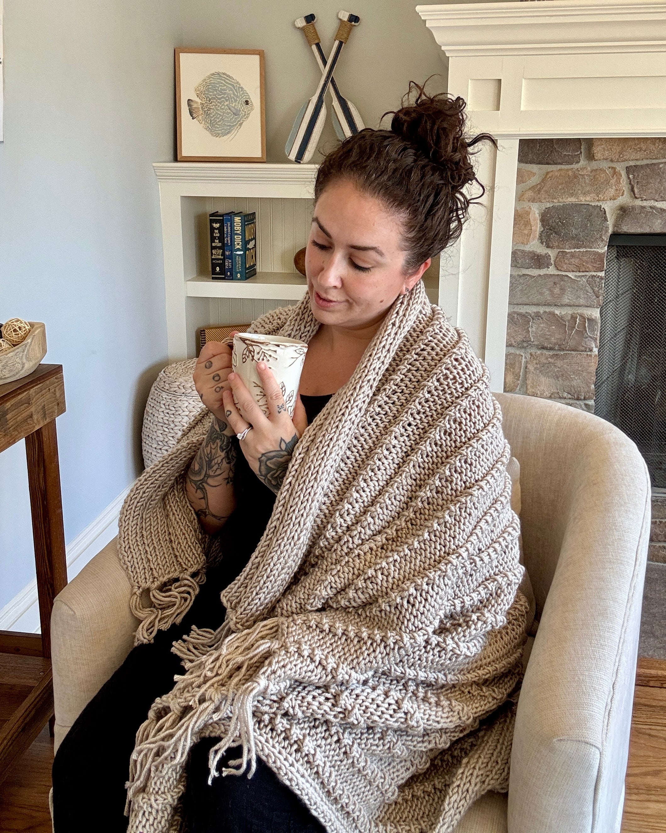 Woman sitting in a cozy living room holding a mug wrapped in a blanket.