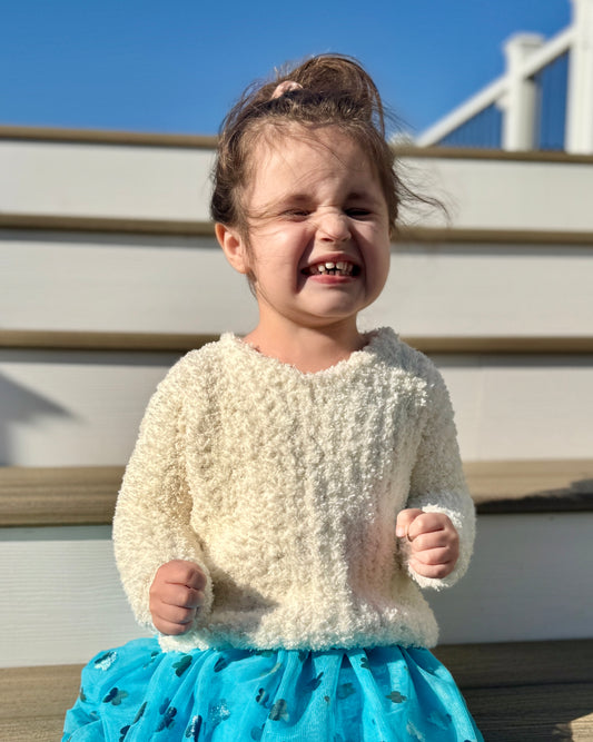 Child wearing a textured white sweater and blue skirt outdoors